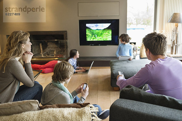 Familie mit elektronischen Geräten im Wohnzimmer