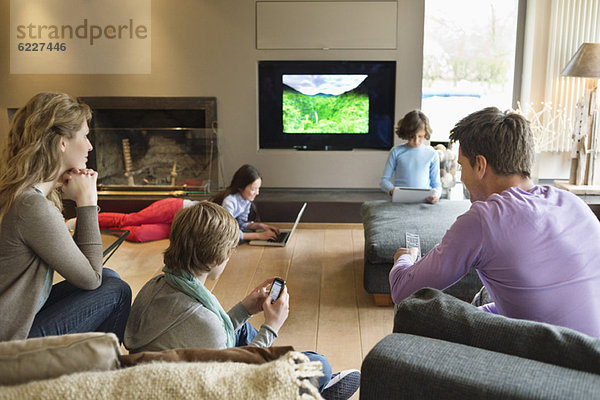 Familie mit elektronischen Geräten im Wohnzimmer