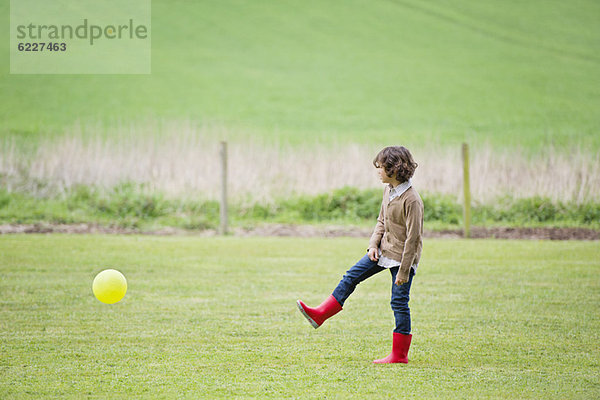 Junge spielt mit einem Ball auf einem Feld