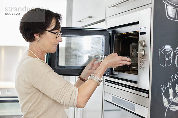 Ältere Frau stellt ein Tablett in den Ofen