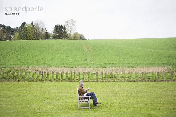 Mann  der auf der Bank sitzt und ein Handy auf dem Feld benutzt.