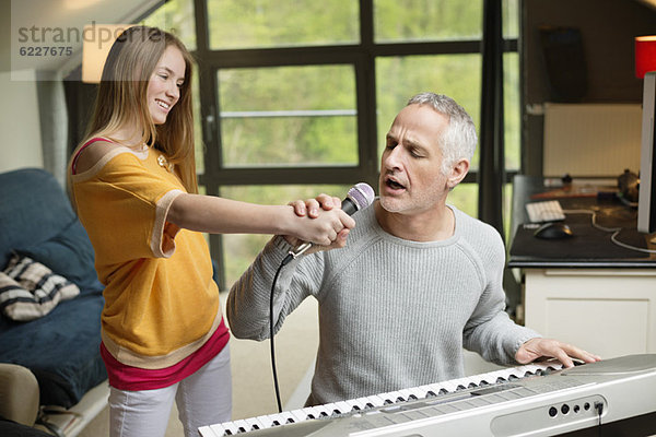 Mann singt und spielt mit seiner Tochter zu Hause Klavier.