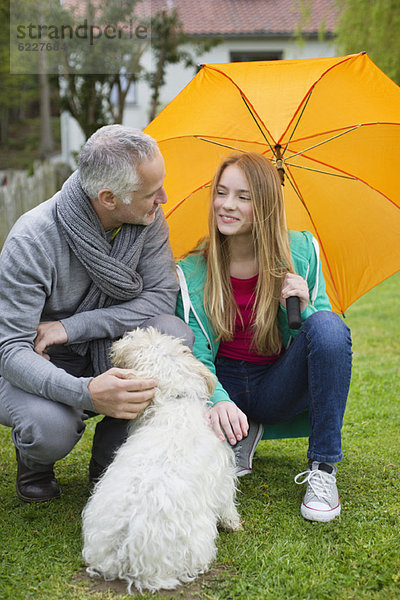 Mann mit seiner Tochter beim Verwöhnen eines Hundes im Rasen