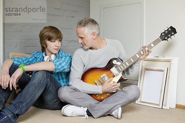 Mann  der mit seinem Sohn zu Hause Gitarre spielt.