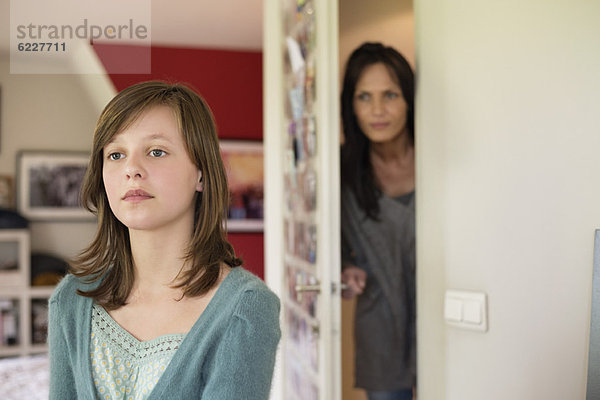 Frau beobachtet ihre Tochter hinter der Tür im Schlafzimmer
