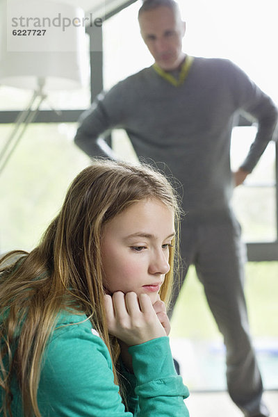 Ein Mädchen sieht verärgert aus  wenn ihr Vater neben ihr steht.