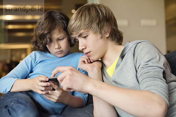 Teenager-Junge mit seinem Bruder  der ein Handy benutzt.