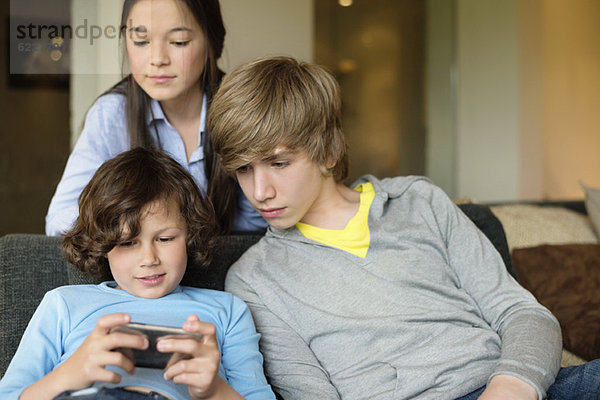 Junge benutzt ein Handy mit seinem Bruder und seiner Schwester zu Hause.