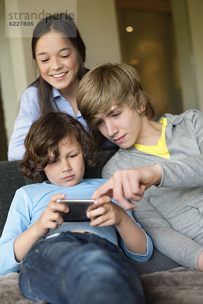 Junge benutzt ein Handy mit seinem Bruder und seiner Schwester zu Hause.