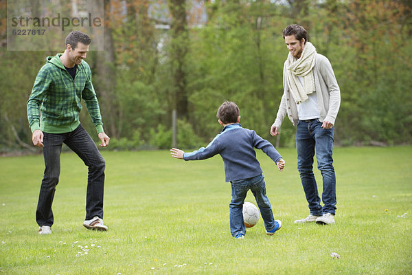 Junge spielt Fußball mit zwei Männern im Park