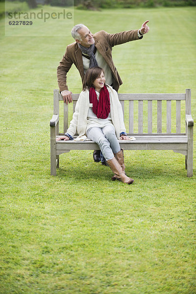 Mann sitzt mit seiner Tochter auf einer Bank und zeigt in einen Park.