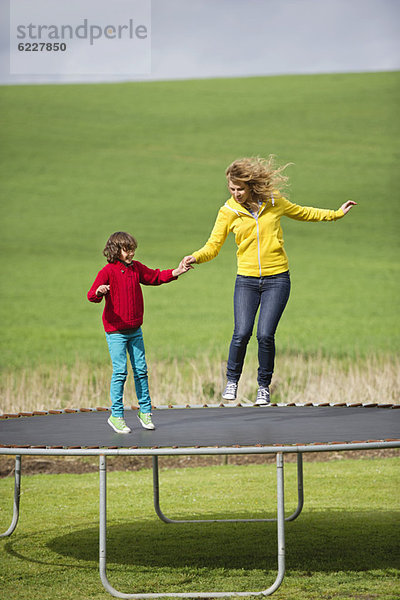 Frau mit ihrem Sohn  der auf einem Trampolin auf einem Feld springt.