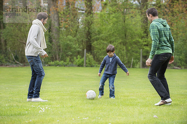 Junge spielt Fußball mit zwei Männern im Park