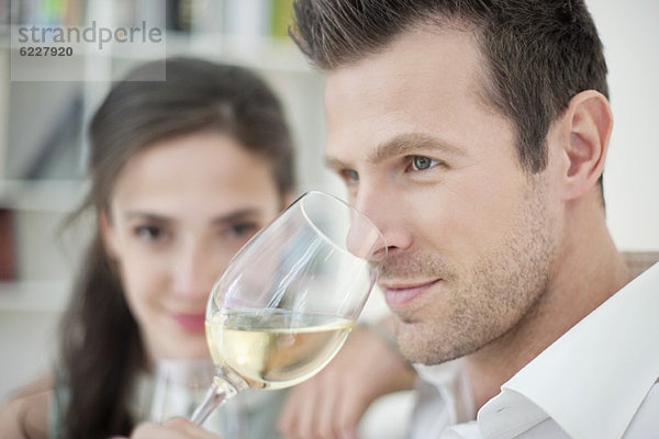 Mann trinkt Weißwein mit seiner Frau im Hintergrund