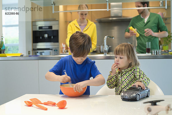 Kleines Mädchen mit einem Spielzeugauto  das seinen Bruder beim Kochen in der Küche beobachtet.