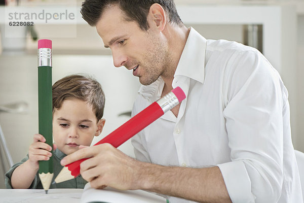 Mann und Sohn schreiben mit großen Bleistiften