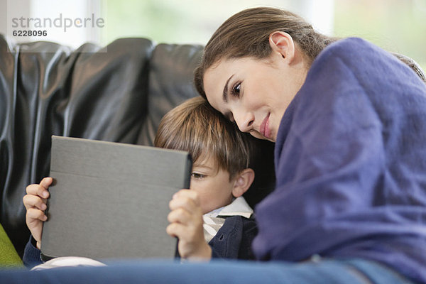 Frau  die ihren Sohn mit einem digitalen Tablett ansieht.