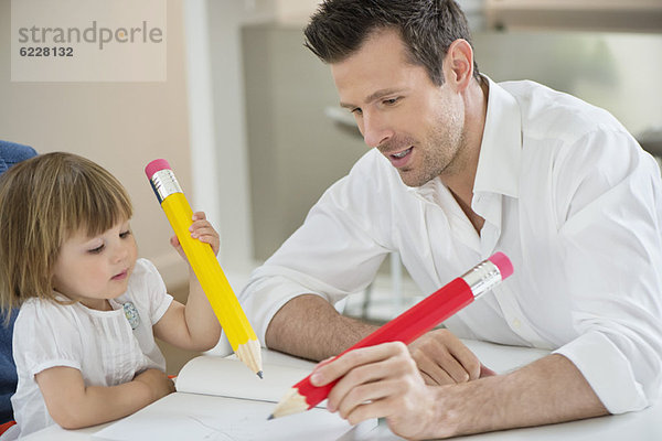 Mann und Tochter schreiben mit großen Bleistiften