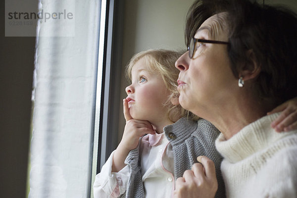 Frau mit ihrer Enkelin beim Blick durchs Fenster