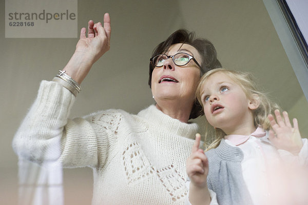 Frau mit ihrer Enkelin beim Blick durchs Fenster