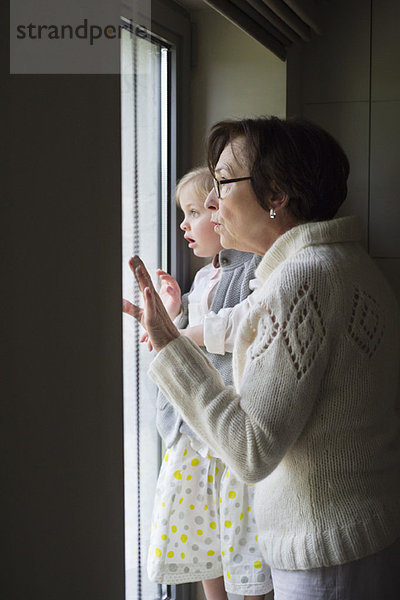 Frau mit ihrer Enkelin beim Blick durchs Fenster