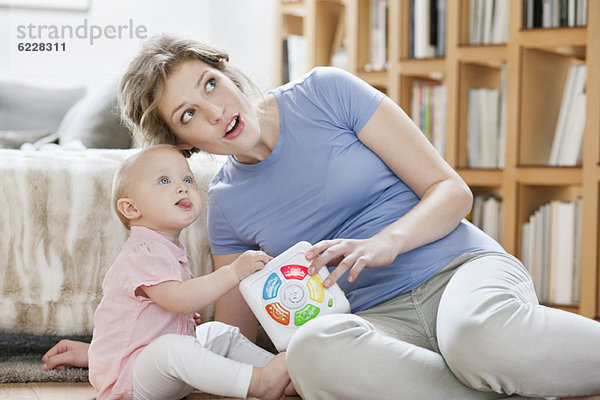 Frau sitzt neben ihrer Tochter und spielt mit einem Spielzeug.