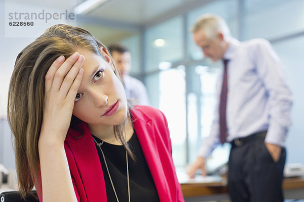Die weibliche Führungskraft sieht traurig aus in einem Büro mit ihren Kollegen  die im Hintergrund diskutieren.