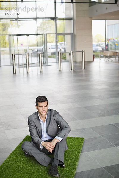 Geschäftsmann entspannt auf Grasmatte in einer Bürolobby
