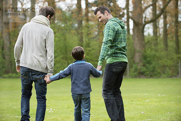 Rückansicht eines Jungen  der mit zwei Männern in einem Park spazieren geht.