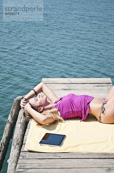 Blonde junge Frau liegt auf einem Steg am See