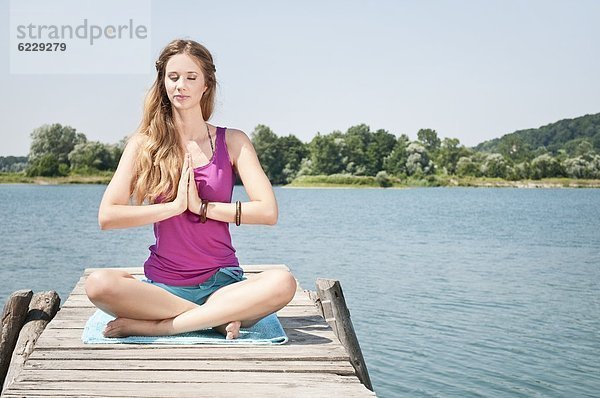 Blonde junge Frau macht Yoga an einem See