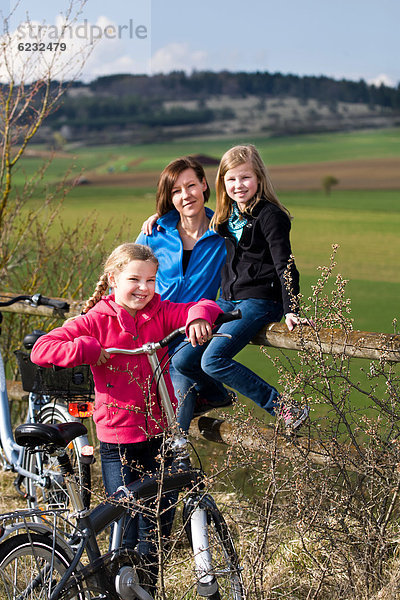 Mutter und zwei Töchter mit Fahrrädern in ländlicher Umgebung
