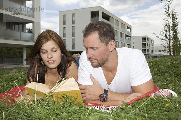 Junges Paar liegt auf einer Wiese und liest ein Buch