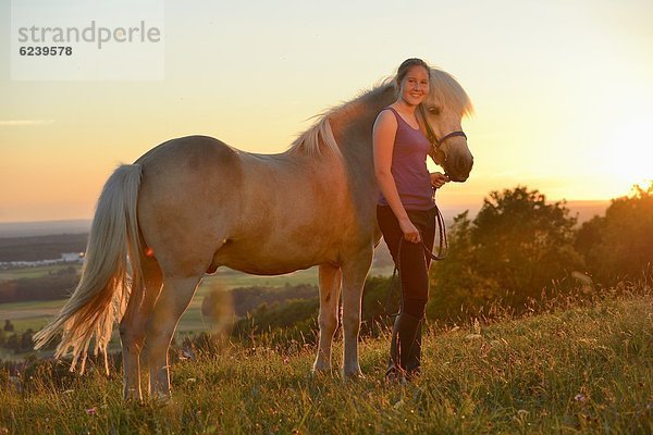 Mädchen mit Pferd auf einer Wiese bei Sonnenuntergang