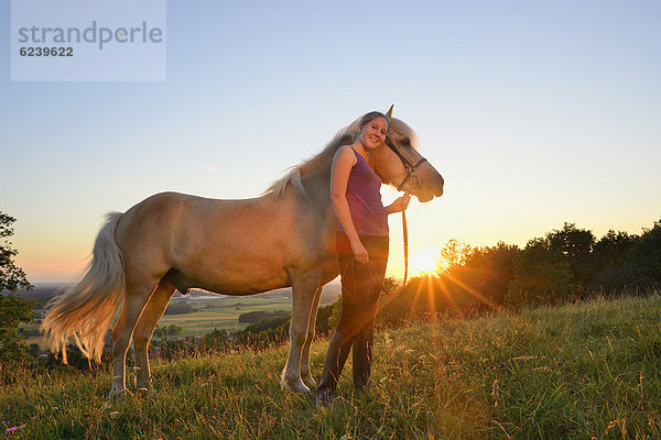 Mädchen mit Pferd auf einer Wiese bei Sonnenuntergang