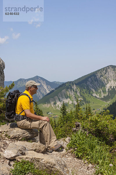 56jähriger Wanderer sitzt auf Felsen und genießt die Aussicht  Taubenstein bei Spitzingsee  Alpen  Mangfallgebirge  Bayern  Deutschland  Europa