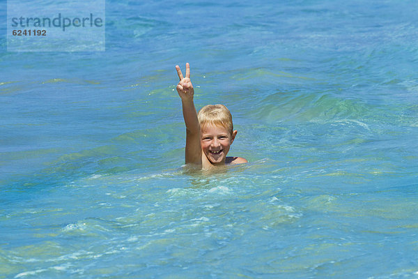 Ein Junge  8 Jahre  badet lachend im Meer  macht V-Zeichen