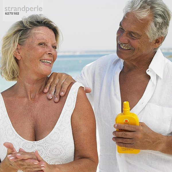 Senior couple on beach  man applying suncream to woman