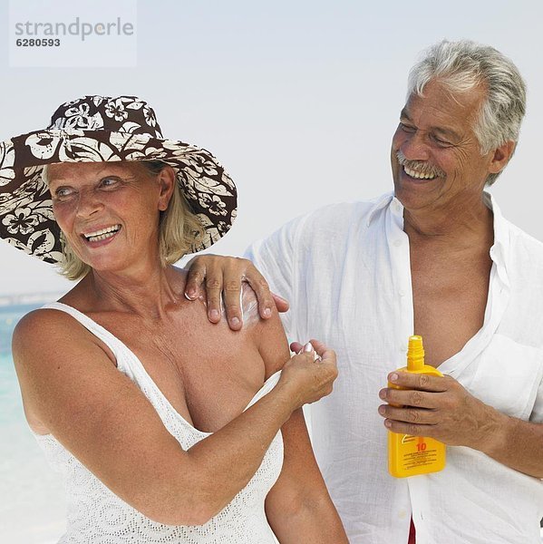 Senior couple on beach  man applying suncream to woman