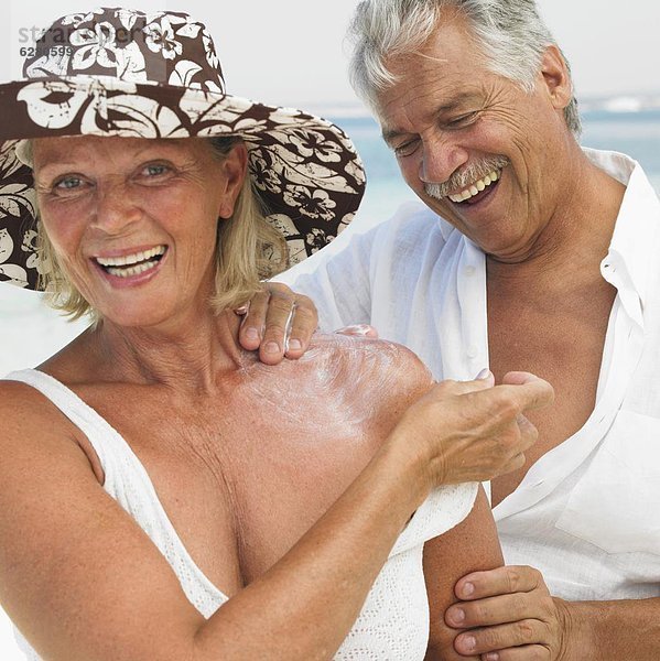 Senior couple on beach  man applying suncream to woman