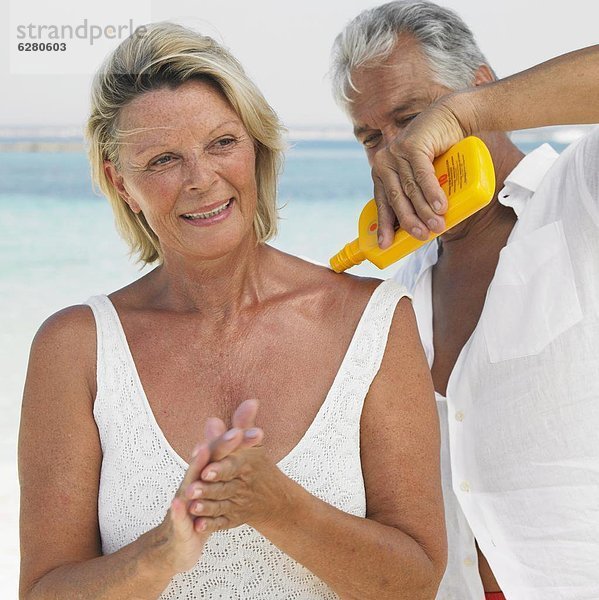 Senior couple on beach  man applying suncream to woman