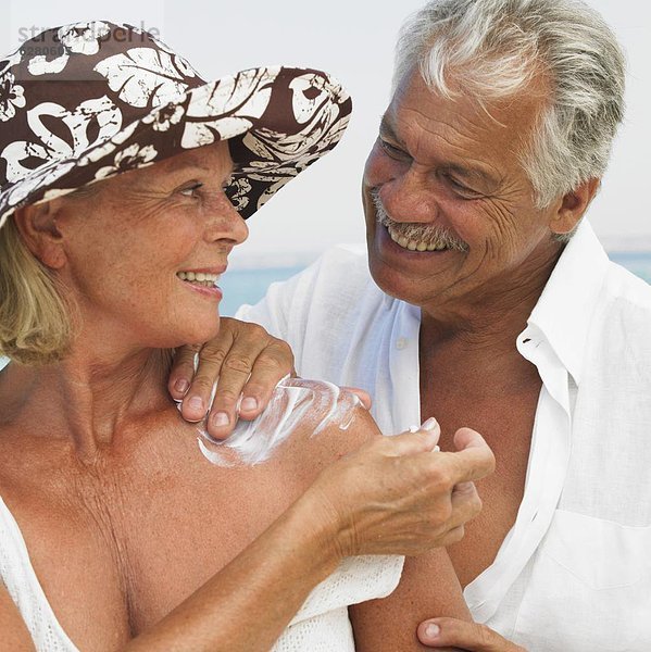 Senior couple on beach  man applying suncream to woman