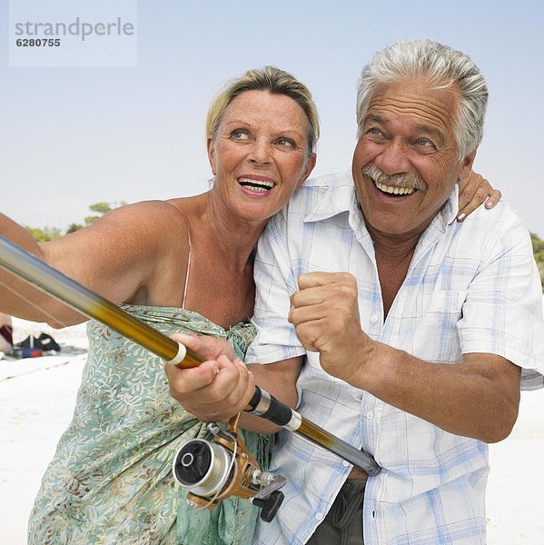 Senior couple on beach  man holding fishing rod