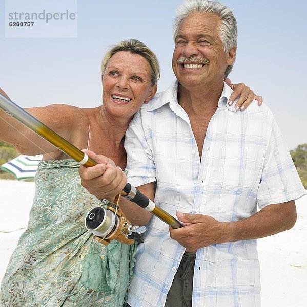 Senior couple on beach  man holding fishing rod