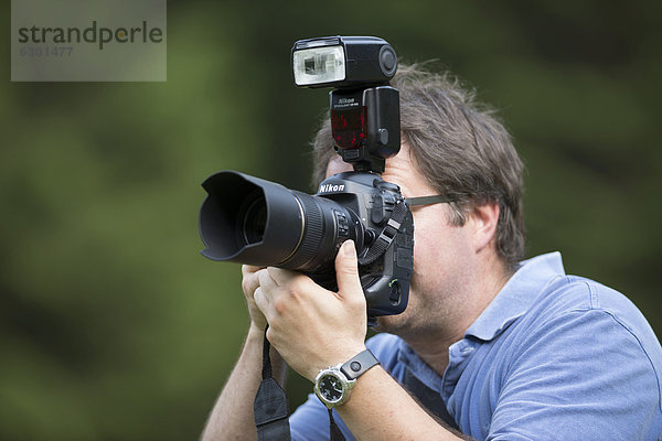 Fotograf  Mitte 40  fotografiert  blickt durch den Sucher einer digitalen Spiegelreflexkamera Nikon D4 mit Aufsteckblitz
