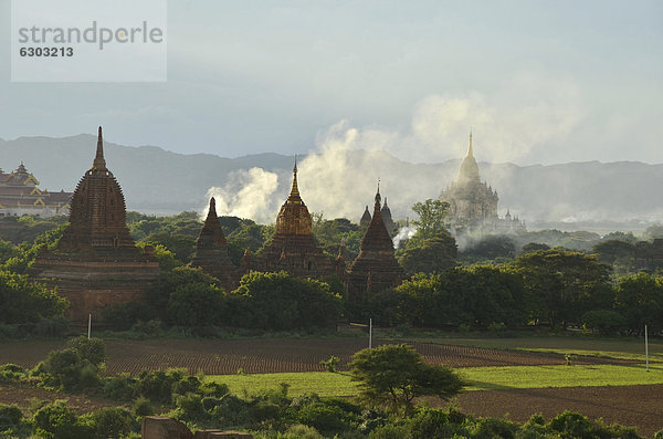 Aufsteigender Rauch  Nebel im Abendlicht zwischen den Feldern  Tempel und Pagoden  Ananda Tempel und Thatbyinnyu Tempel  Bagan  Myanmar  Burma  Birma  Südostasien  Asien