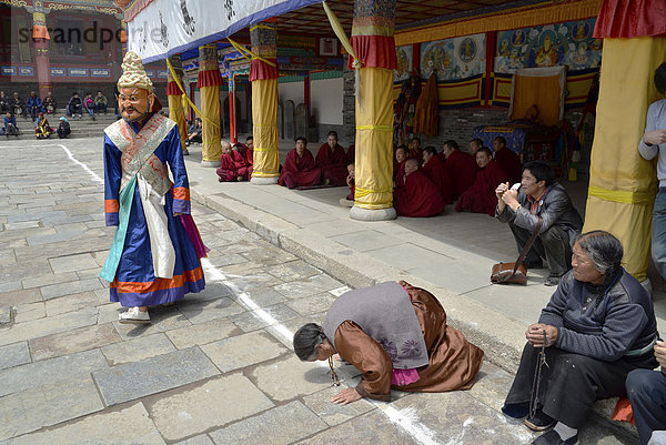 Tibetischer Buddhismus  Frau kniet betend nieder zu religiösem Maskentanz Cham Tanz im bedeutenden Gelugpa-Kloster Kumbum  Ta'er Kloster  Huangzhong  Xinning  Qinghai  ehemals Amdo  Tibet  China  Asien