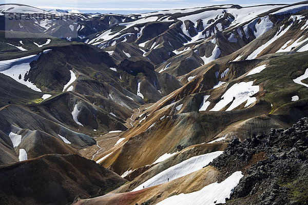 Wanderer auf Wanderweg  Blick vom Vulkan Brennisteinsalda auf schneebedeckte Rhyolith-Berge  Landmannalaugar  Fjallabak Naturschutzgebiet  Hochland  Island  Europa