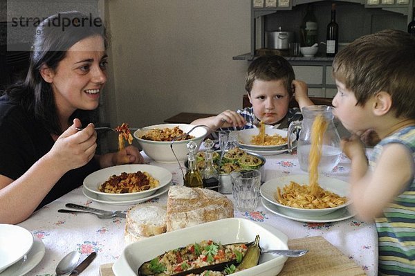 Mutter mit zwei Kindern sitzen am Tisch & essen Tagliatelle
