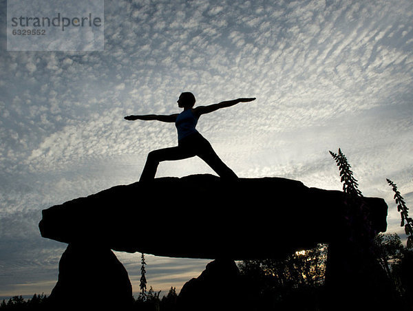 Silhouette der Frau in Krieger-Yoga-Pose auf einem Felsen